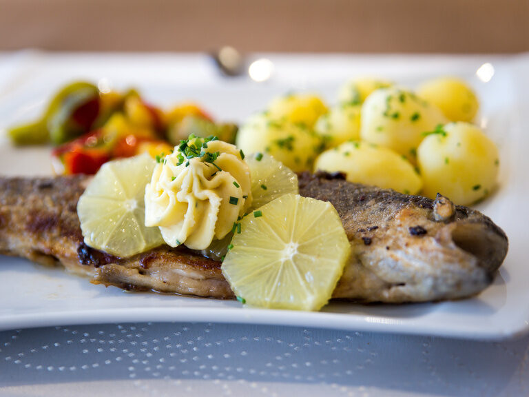 Auf einem Teller ist Fisch mit Kartoffeln und Gemüse angerichtet